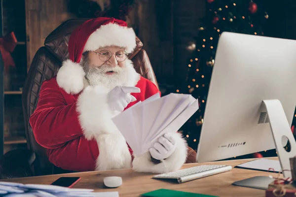 Foto grijs haar santa claus zitten tafel voor te bereiden x-mas kerst nacht middernacht ontvangen verlanglijstje brieven tellen enveloppen vingers in huis nieuwjaar geest ornament dragen pet hoofddeksel — Stockfoto