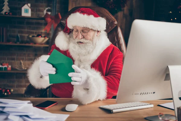 Foto van grappige vrolijke hulst santa claus x-mas kerstman zittafel open envelop lees wensenlijst brief in huis binnen met nieuwjaar advent ornament dragen rood kostuum — Stockfoto