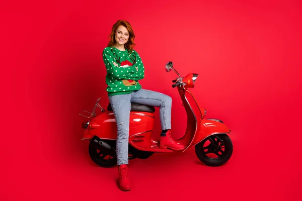 Foto retrato de motociclista confiante sentado em scooter com os braços dobrados vestindo suéter verde feio isolado em fundo colorido vermelho vívido — Fotografia de Stock