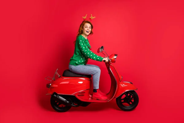 Zdjęcie portret boczny widok kobiety jazda skuter noszenie zielony skoczek jeleń zabawki nakrycia głowy izolowane na żywe czerwone tło — Zdjęcie stockowe