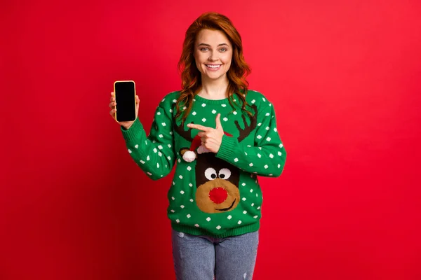 Portrait photo de femme pointant du doigt le téléphone avec un copyspace portant un pull vert laid avec des rennes isolés sur un fond rouge vif — Photo