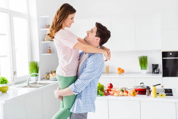 Profil vue de côté portrait de son il il elle deux agréable attrayant affectueux joyeux joyeux conjoints passer des vacances en s'amusant gars portant fille dans la lumière blanc intérieur cuisine maison appartement — Photo