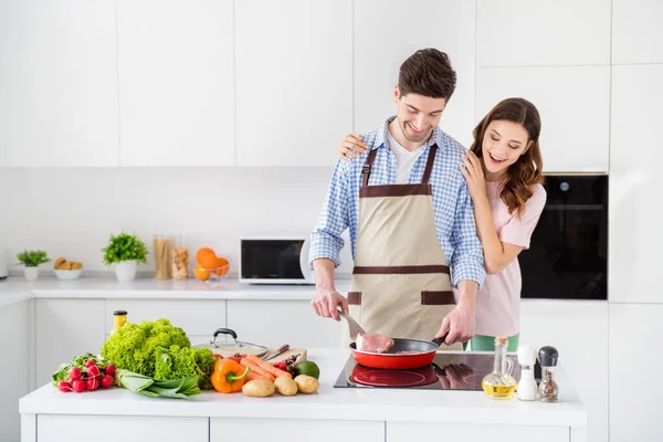 Портрет двух привлекательных и заботливых, радостных и веселых супругов, готовящих домашнюю еду, проводящих выходные в светло-белой квартире на кухне в помещении — стоковое фото