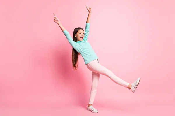 Plná délka tělo velikost fotografie hravé malé dívky ukazující nahoru s prsty krok vpřed s úsměvem izolované na růžovém pozadí — Stock fotografie