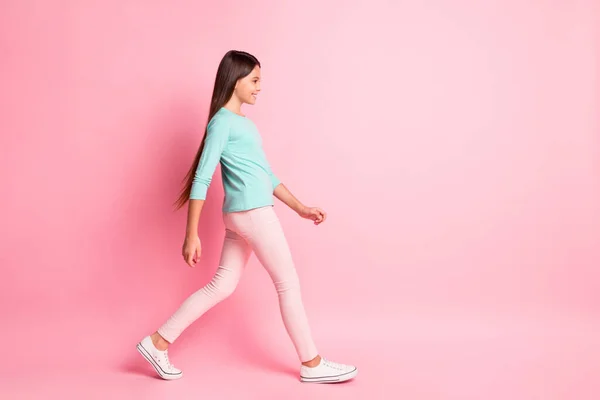 Foto de perfil de tamaño completo del cuerpo de la encantadora señora latina pequeña dulce largo peinado caminar mirada espacio vacío sonrisa usar pantalones de sudadera turquesa zapatillas blancas aislado color rosa fondo — Foto de Stock