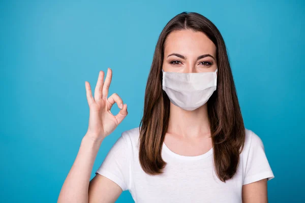 Portret van positieve vrolijke meisje show oke teken covid quarantaine aanwezig advertenties promotie dragen goed kijken medisch masker kleding geïsoleerd over blauwe kleur achtergrond — Stockfoto