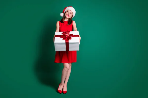 Full length photo positive girl in santa claus headwear celebrate x-mas christmas newyear party give big gift box friend wear stilettos high-heels skirt isolated green color background