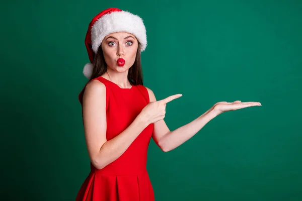Fotografie roztomilé dáma poslat vzduch polibek držet otevřené paže dlaně přímý prst prodej sleva novoroční adventní nákupní produkt oblečení x-mas sníh dívka kostým šaty Santa čepice izolované zelené barvy pozadí — Stock fotografie