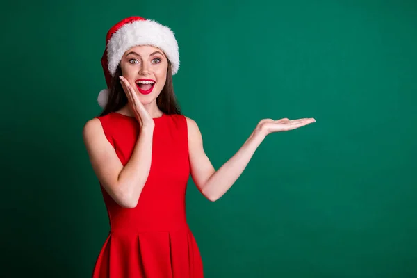 Foto de encantadora señora sorprendida divertida mantenga abierta la palma del brazo newyear venta descuento decoración producto adicto comprador desgaste x-mas traje de niña de nieve vestido de santa gorra aislado color verde fondo — Foto de Stock