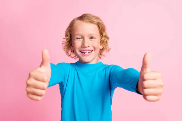 小男孩举起两个大拇指的照片象征着笑着穿上蓝色的套头毛衣孤立的粉红色背景 — 图库照片