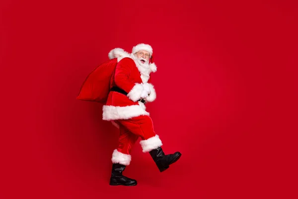 Foto portret van verbaasd santa claus met open mond dragen enorme zak met geschenken geïsoleerd op felrood gekleurde achtergrond — Stockfoto