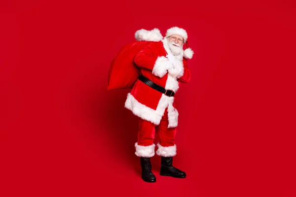 Foto portret van de kerstman dragen grote zak met geschenken geïsoleerd op levendige rood gekleurde achtergrond — Stockfoto