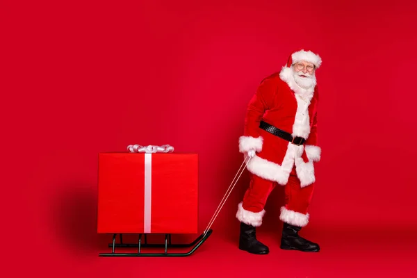 Photo portrait of trendy funky santa claus pulling sleigh with big box on it isolated on vivid red colored background — Stock Photo, Image