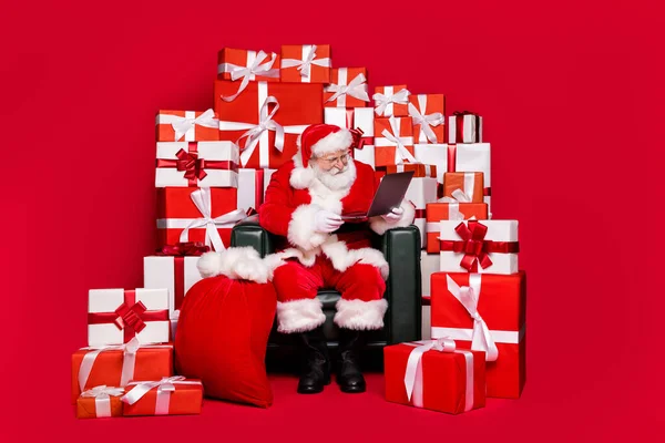 Full length body size view of his he nice handsome bearded focused Santa sit in chair reading e-mail wish list North Pole order delivery isolated bright vivid shine vibrant red color background — Stockfoto