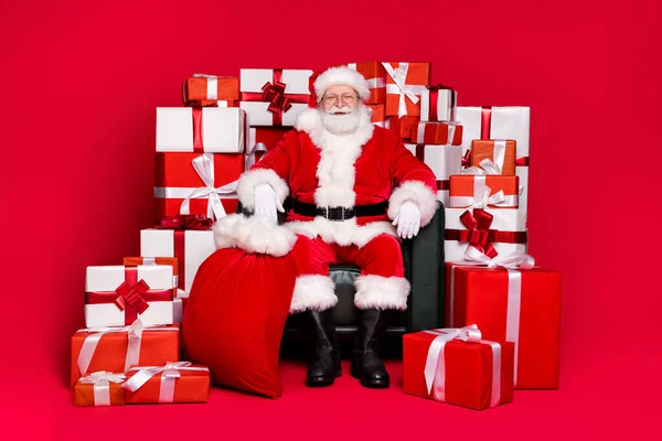 Full length body size view of his he handsome fat overweight cheerful Santa Saint Nicholas sitting in chair pile stack giftboxes isolated bright vivid shine vibrant red color background — Stock Photo, Image