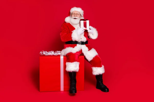 他那英俊肥胖、肥胖、快乐的圣诞老人的全身上下全貌坐在巨大的礼品盒上，欢度佳节佳节，与外界隔绝，灯火通明，色彩艳丽的红色背景 — 图库照片