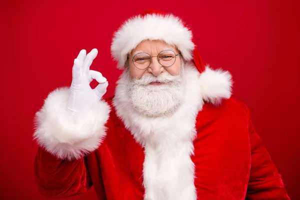 养老金领取者爷爷灰白胡子举起手，露出亲切的微笑，确保你及时送来礼物穿上圣诞装束白色手套外套眼镜头戴孤立的红色背景 — 图库照片