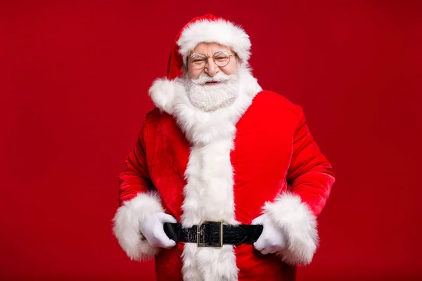 Photo of retired old man grey beard hand hip cheerful self-assured wait last days before newyear wear santa costume leather belt gloves coat spectacles headwear isolated red color background — Stock Photo, Image