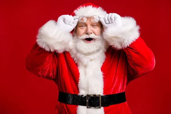 Foto van gepensioneerde oude man grijze baard take off hold specs glimlach opgewonden glimlach cant geloven kerst wonder dragen kerstman kostuum riem handschoenen jas bril hoofddeksel geïsoleerde rode kleur achtergrond — Stockfoto