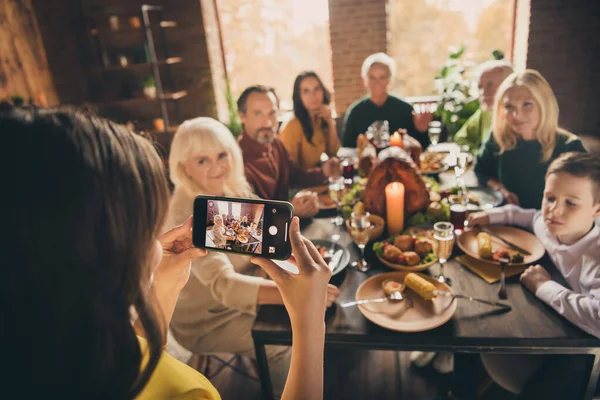 Fotografie plné rodiny shromáždění osm lidí malý fotograf dcera držet telefon, aby portrét zapamatovat moment večeře velký stůl krůty generace doma večer obývací pokoj uvnitř — Stock fotografie