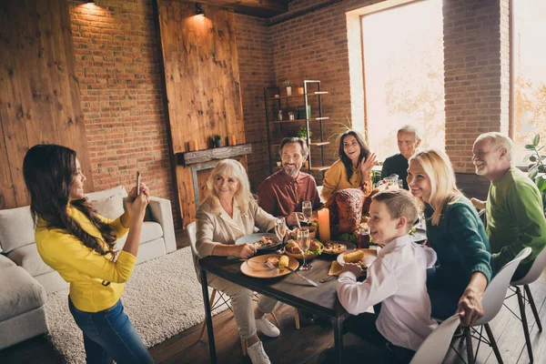 Photo of full family gathering eight people small daughter hold telephone make picture harmonic holiday mother wave hand dinner big table turkey generation home evening living room indoors