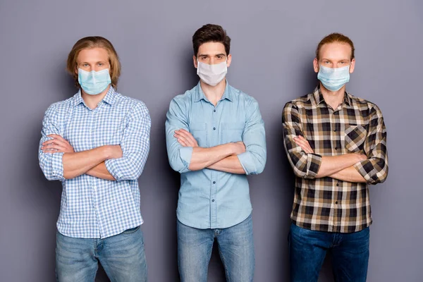 Retrato de três caras masculinos sérios melhor amigo companheiro corona vírus equipe de luta braços dobrados usar máscara médica isolada sobre fundo cor pastel cinza — Fotografia de Stock