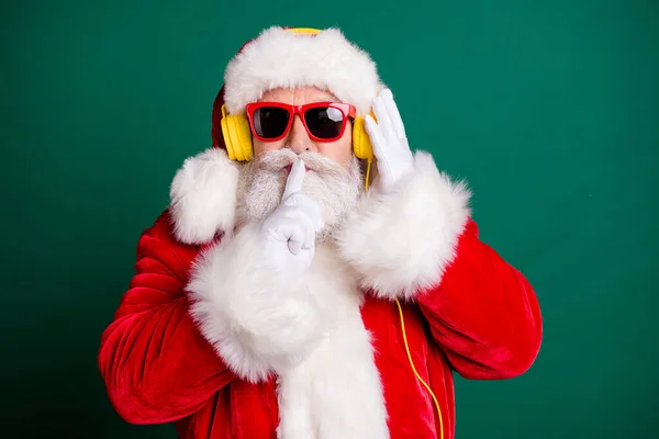 Close-up portrait of his he nice attractive handsome Santa father listening pop music bass single wearing fluffy gloves showing shh sign conspiracy secret isolated over green color background — Stock Photo, Image