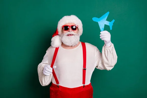 Portrait of his he nice handsome cheerful funky fat overweight Santa holding in hand paper plane shape tour resort having fun destination airline isolated over green color background — Stock Photo, Image