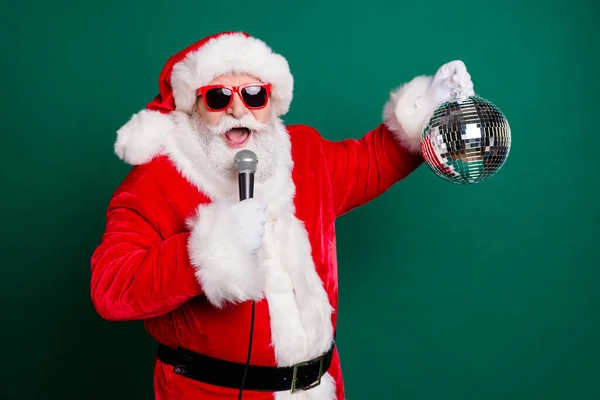 Portrait of his he nice attractive handsome cheerful bearded Santa star mc pj grandfather singing pop hit single having fun holding silver glossy ball Eve Noel isolated over green color background — Stock Photo, Image