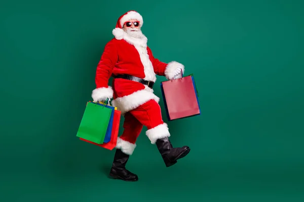 Tam boy vücut ölçüsü. Şişko, neşeli, Noel Baba 'nın bir şeyler taşıdığı yeşil arka planda izole edilmiş Noel hediyeleri. — Stok fotoğraf