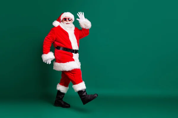 Helkropps profil foto av pensionär farfar promenader galleria korridorer hälsning butik kunder bära röd Santa kostym päls handskar solglasögon huvudbonad isolerad grön färg bakgrund — Stockfoto