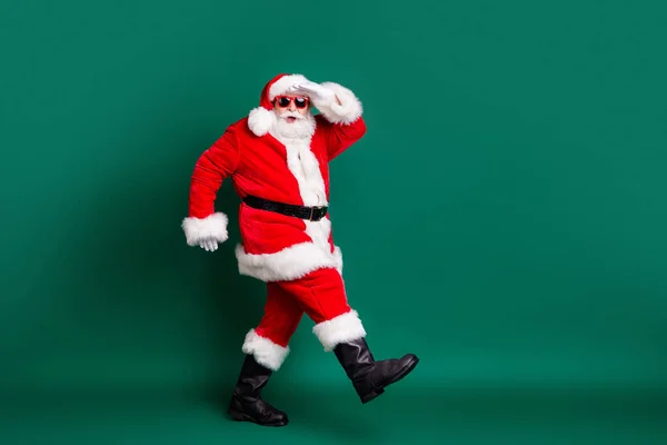 Full body size profile photo of pensioner grandpa funny walking journey north pole after x-mas eve wear red santa costume coat gloves sunglass cap isolated green color background