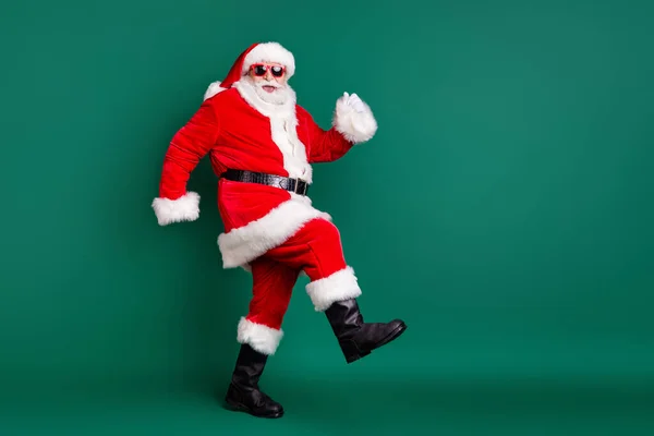 Full body size profil zdjęcie emerytowanego dziadka zabawny spacer razem elfy jelenie kupić prezent dla dzieci nosić czerwony Santa kostium płaszcz rękawiczki czapka słoneczna odizolowany zielony kolor tło — Zdjęcie stockowe