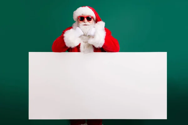 Photo of retired confident grandpa white empty board offer interesting newyear product novelty wear red santa costume coat gloves sunglass headwear isolated green color background — Stock Photo, Image