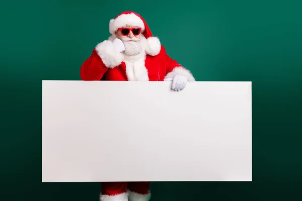 Foto de abuelo confiado retirado mantenga la tabla vacía blanca ofrecen increíble propuesta de año nuevo desgaste traje de santa rojo guantes abrigo sunglass headwear aislado color verde fondo — Foto de Stock