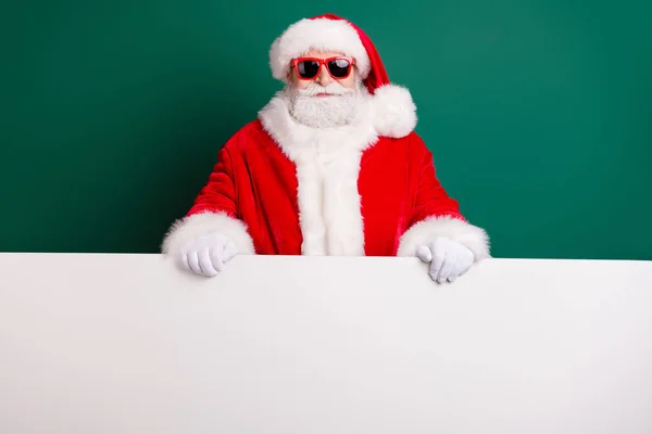 Foto de pensionista elegante abuelo pelo gris barba celebrar pizarra blanca la promoción de la línea actual limitada desgaste traje de santa roja guantes abrigo gafas de sol diadema aislado color verde fondo — Foto de Stock