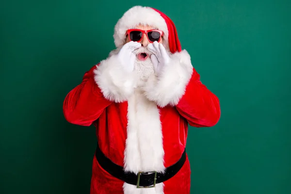 Foto di pensionato nonno bianco barba mani bocca aperta urlando promuovere il nuovo anno negozio indossare rosso Santa x-mas costume cappotto guanti occhiali da sole cintura copricapi isolato colore verde sfondo — Foto Stock