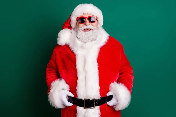Photo of retired grandpa white beard smiling hands belt check deer prepare journey north pole wear red santa costume coat gloves sunglass headwear isolated green color background — Stock Photo, Image
