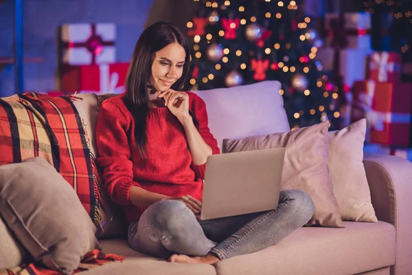 소파에 앉아 크리스마스 장식을 하고 노트북을 둘러보는 사려깊은 여성의 사진 — 스톡 사진