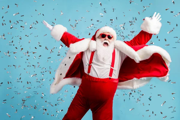 Zdjęcie emeryta starzec szary broda beztroski podnieść ręce taniec otwarte usta udawać latający anioł confetti nosić Santa X-mas kostium szelki okulary przeciwsłoneczne pojedynczy niebieski kolor tło — Zdjęcie stockowe