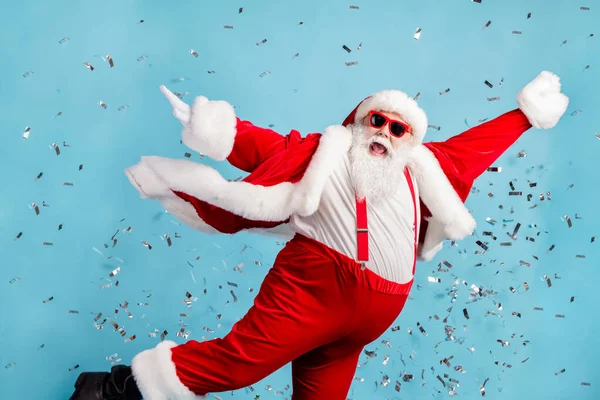 Foto di pensionato vecchio uomo grigio barba spensierato sollevare le mani volare posa danza partito pronto saltare piscina coriandoli usura Santa x-mas costume bretella occhiali da sole copricapi isolato colore blu sfondo — Foto Stock