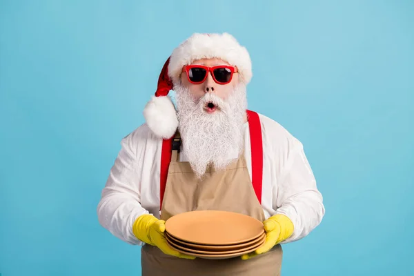 Zdjęcie emeryta starzec szary broda trzymać czyste dania szok zobacz klienta niezadowolony nosić Santa x-mas kostium fartuch gumowe rękawiczki szelki sunglass czapka odizolowany niebieski kolor tło — Zdjęcie stockowe