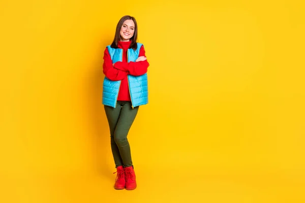 Pleine longueur photo de mignonne belle jeune dame souriant mains pliées regard assuré attendre le temps de ski porter pantalon vert gilet bleu bottes pull rouge isolé couleur jaune vif arrière-plan — Photo