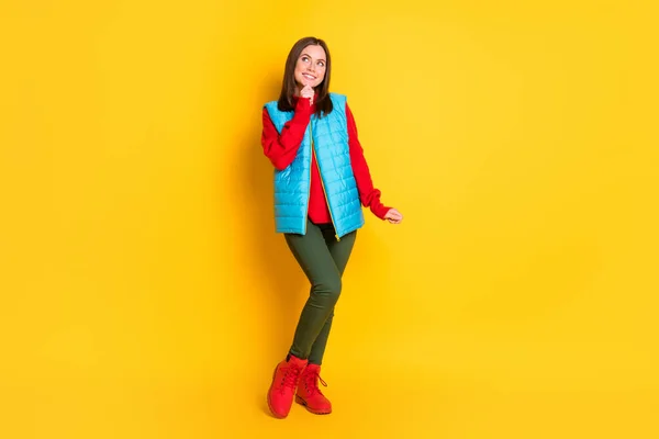 Corpo inteiro tamanho foto de muito bonito jovem senhora sonhadora olhar vazio espaço mão queixo sorridente menina posando desgaste verde calças azul colete vermelho botas isoladas cor amarela brilhante fundo — Fotografia de Stock