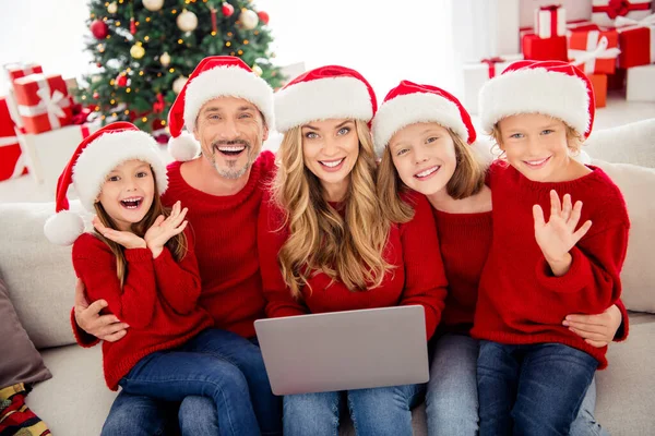 Full family x-mas noel event. People mommy daddy little kids sit sofa hold laptop tradition video chat spirit congratulations wear santa claus caps in house indoors with christmas tree — Stock Photo, Image