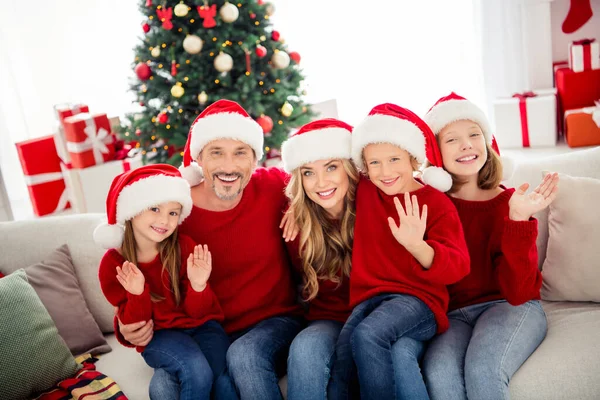 Rodinný vánoční čas snů. Lidé maminka maminka táta tatínek a malé předpuberťáci sedět pohovky na gauči vlny ruce pozdravit novoroční nosit Santa Claus čepice v domě vnitřní s vánoční dekorace — Stock fotografie