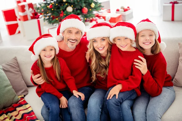 Véspera de espírito de x-mas de família completa. Pessoas mãe mamãe papai papai e três crianças pequenas pré-adolescentes sentar sofá desgaste santa claus cap em casa dentro de casa com árvore de natal sonho ornamento — Fotografia de Stock