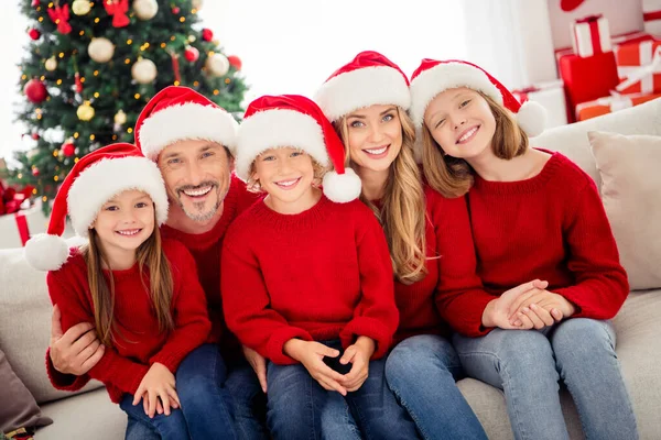 Volle familie mensen kerstmis bijeenkomst. Mama papa papa mama en drie kleine tieners zitten sofa dragen kerstman hoofddeksel in huis met traditie noel decoratie — Stockfoto