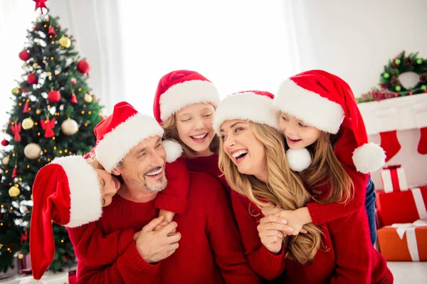 Tam aile noel arifesi toplanması. Küçük çocuklar kucaklaşır, anne baba baba kucaklaşır anne evde Noel Baba şapkası takar ve Noel Baba süsü takar. — Stok fotoğraf