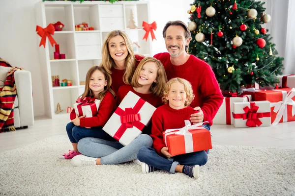 Foto van volle grote familie vijf mensen ontmoeten drie kleine kinderen houden x-mas cadeautjes glanzende glimlach knuffel dragen rode trui jeans in huis woonkamer boom lichten vele geschenkdozen binnen — Stockfoto
